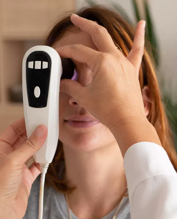 Examen d’iridologie : deux mains tiennent un appareil d’analyse devant l’œil d’une patiente.